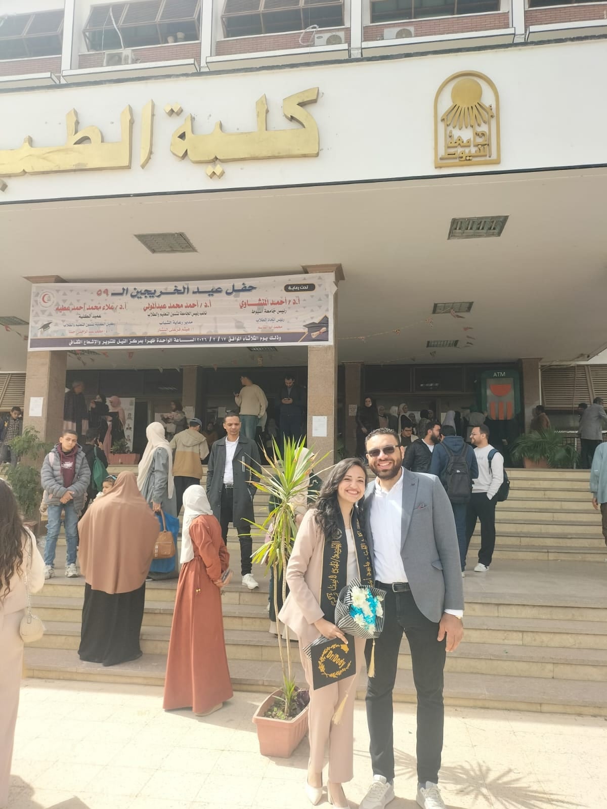 Nada in her graduation sash with John outside her faculty