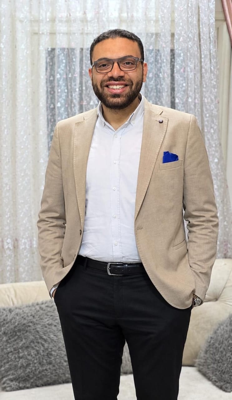 John in a beige blazer and white shirt, smiling