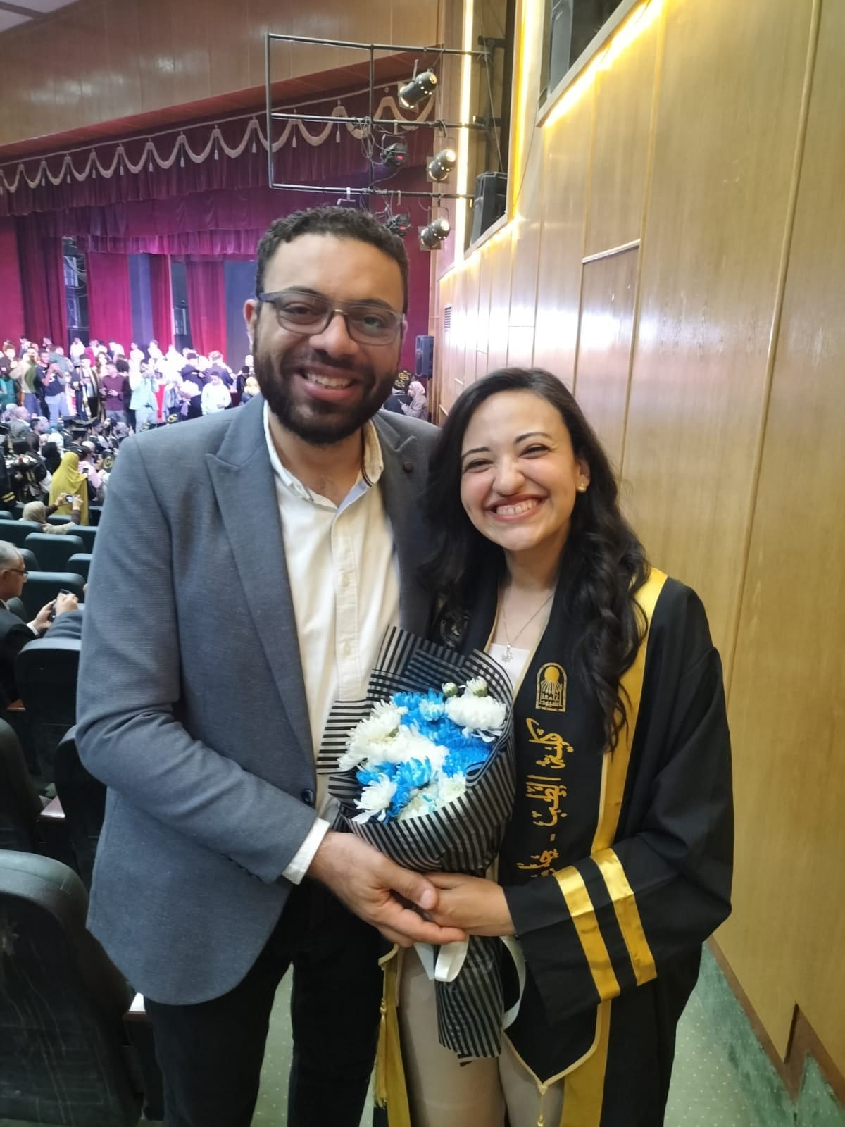 John holding Nada close at her graduation, flowers in her hands